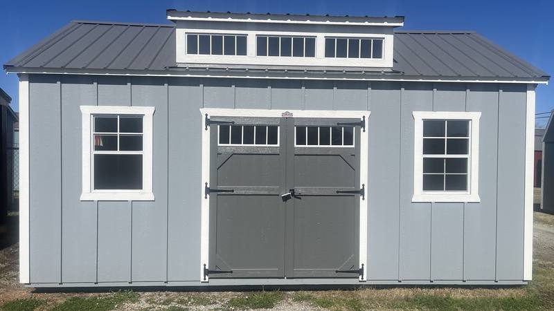 A gray storage building with dark double doors and a dormer roof